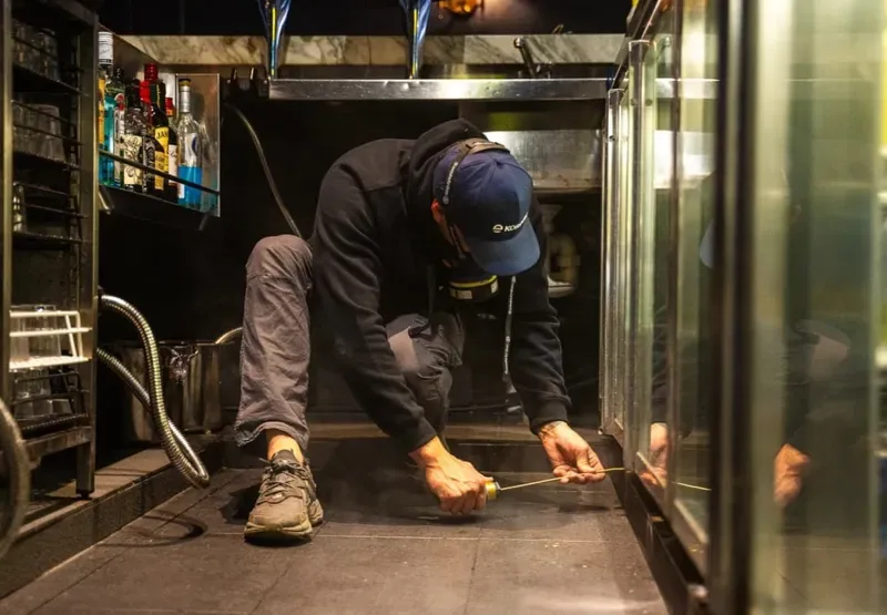 Technician treating under commercial kitchen equipment