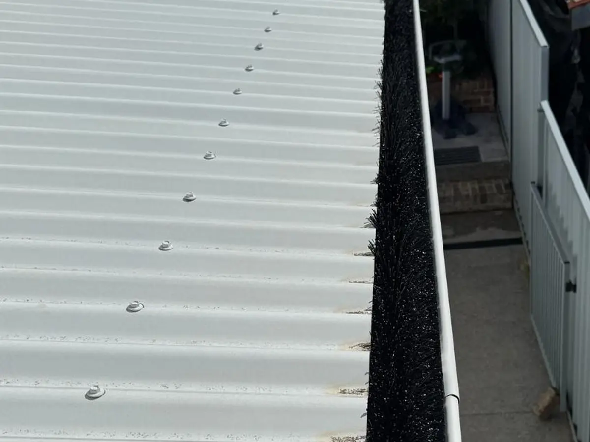 A black gutter brush fitted along the gutter at the edge of a white metal roof.
