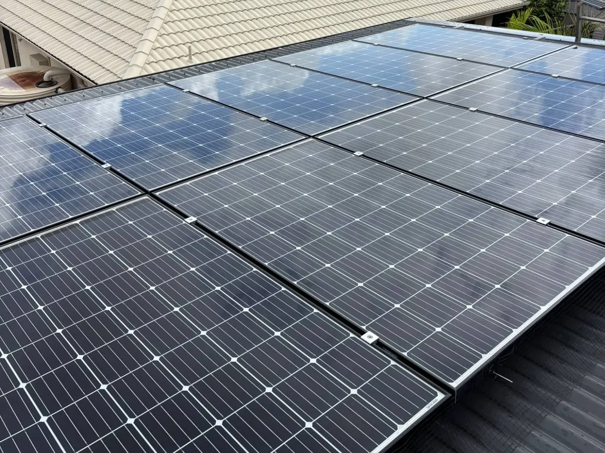 A clean rooftop solar array on a dark metal roof reflecting the sky, next to a cream tiled roof.
