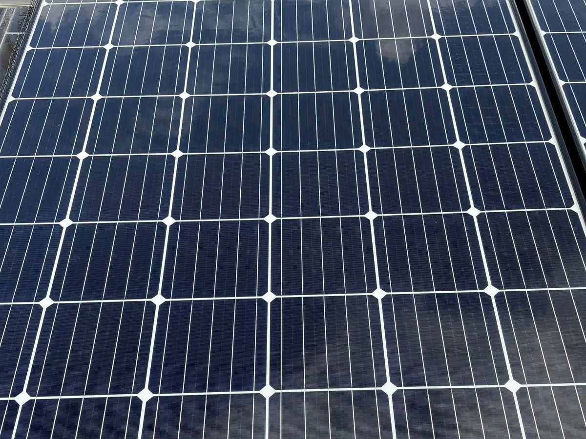 Close-up of a clean, dark blue solar panel with clouds reflected in the glass.